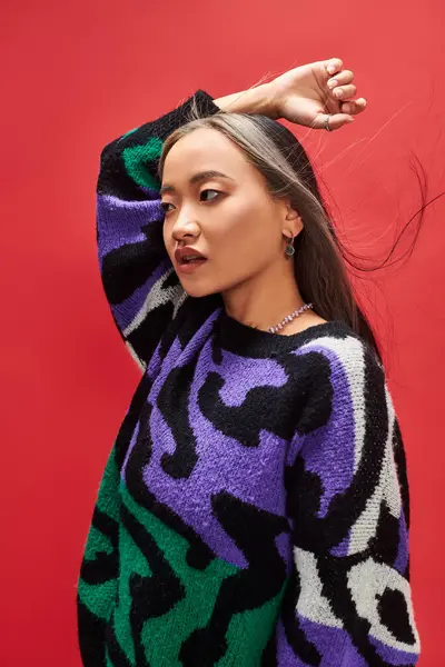 Beautiful and young asian woman in knitted sweater with animal print posing on red background — Stock Photo