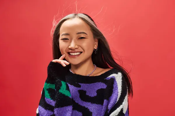 Щаслива молода азіатська жінка в трикотажному светрі з принтом тварин позує на червоному тлі — стокове фото