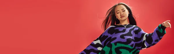 Giovane ragazza asiatica in maglione vibrante con stampa animalier con collana a forma di cuore sul rosso, facilità banner — Foto stock