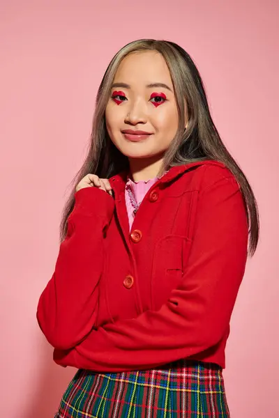 San Valentín concepto de día, alegre mujer asiática con el corazón en forma de maquillaje de ojos sonriendo en rosa telón de fondo - foto de stock