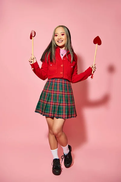Valentines day concept, smiling asian woman with heart shaped eye makeup holding arrows on pink — Stock Photo