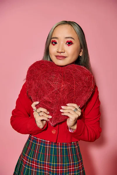 Valentine dia, positivo asiático mulher com vibrante olho maquiagem segurando vermelho coração no rosa pano de fundo — Fotografia de Stock