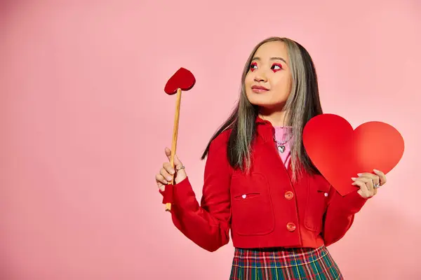 Valentines day, happy asian girl with vibrant eye makeup holding carton heart on pink backdrop — Stock Photo