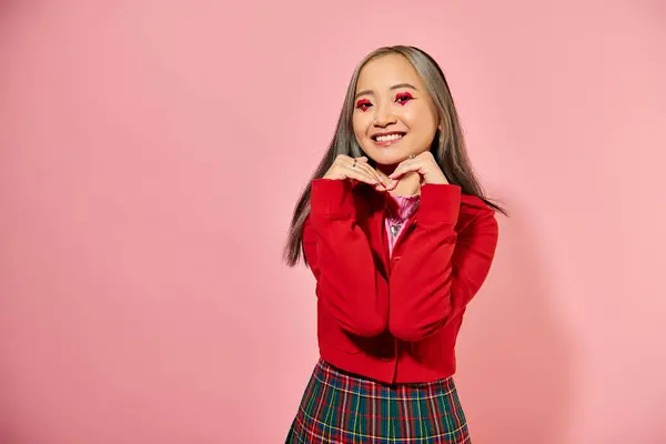 San Valentín día, feliz asiático joven mujer con corazón ojo maquillaje mostrando corazón con las manos en rosa - foto de stock