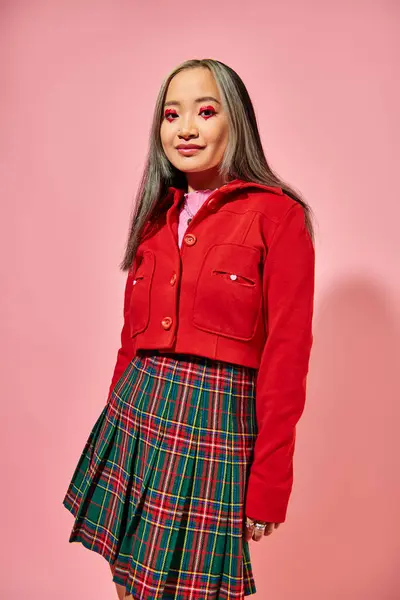 San Valentín día, alegre asiático joven mujer con corazón ojo maquillaje posando en rojo chaqueta en rosa - foto de stock