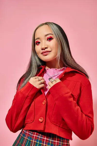 Valentines day, jolly asian young woman with heart eye makeup posing in red jacket on pink — Stock Photo