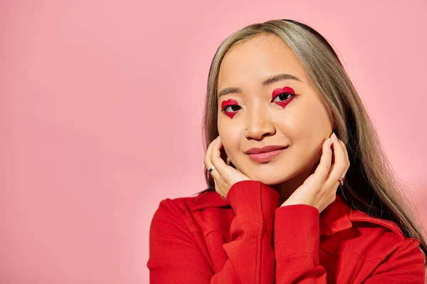 Valentines day concept, cute asian young woman with heart eye makeup posing in red jacket on pink — Stock Photo