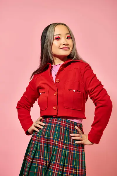 Концепція дня Святого Валентина, щаслива азіатська дівчина в червоній куртці позує руками на стегнах на рожевому тлі — стокове фото