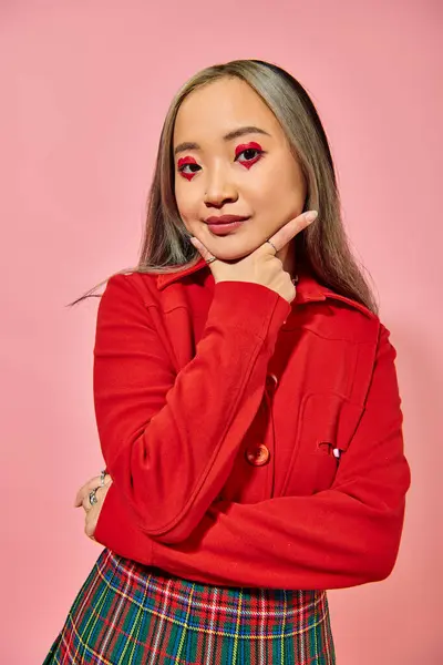 Porträt einer hübschen asiatischen jungen Frau mit herzförmigem Augen-Make-up, die vor rosa Hintergrund in die Kamera blickt — Stockfoto