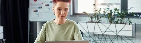 Stylish ambitious queer person with short hair working at laptop in modern office, horizontal banner — Stock Photo