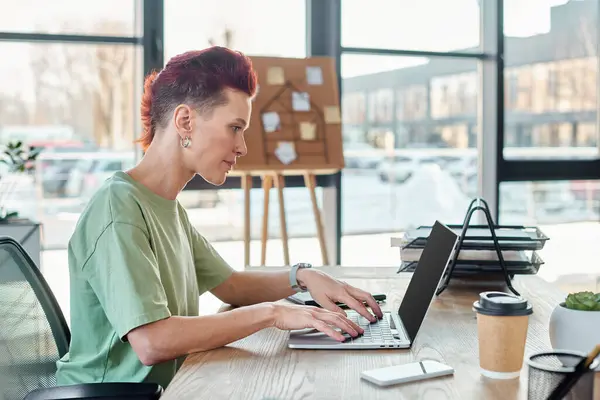 Side view of non-binary person typing on laptop with blank screen near smartphone and coffee to go — Stock Photo