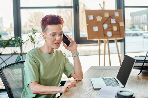 Non-binary business person talking on mobile phone near laptop with blank screen in modern office — Stock Photo