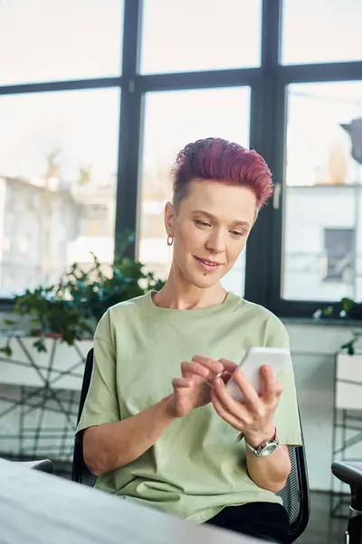 Stylish non-binary individual messaging on mobile phone in contemporary modern office, business — Stock Photo