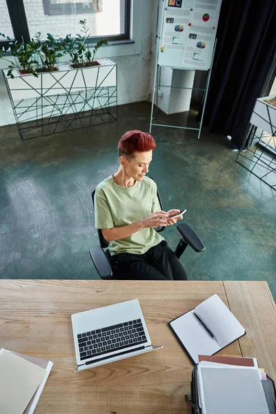 High angle view of queer manager messaging on smartphone near laptop and documents on work desk — Stock Photo