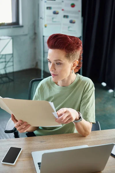 Gerente queer elegante trabalhando com documentos perto de laptop e smartphone com tela em branco no escritório — Fotografia de Stock