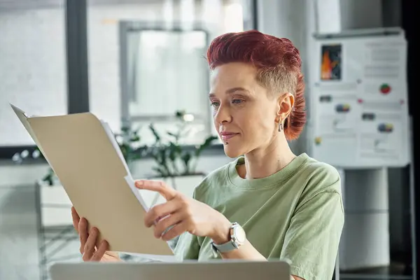 Gérant queer élégant en tenue décontractée avec cheveux courts travaillant avec des documents dans le bureau contemporain — Photo de stock
