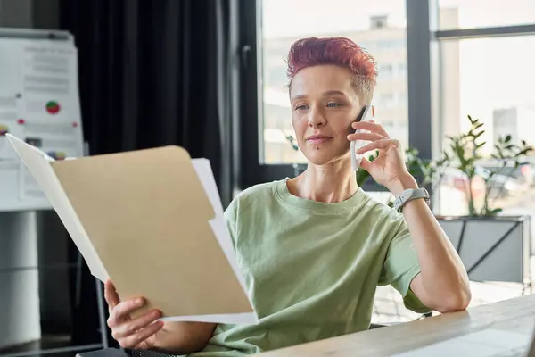 Occupato persona queer parlando su smartphone e guardando i documenti in ufficio moderno, multitasking — Foto stock