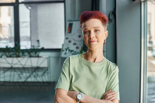 Confident bigender business person with folded arms and looking at camera in office, portrait — Stock Photo