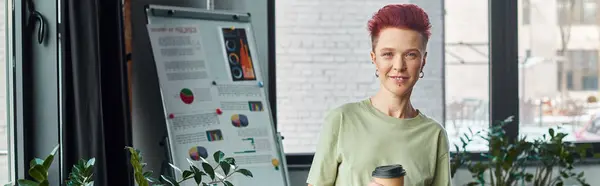 Persona queer sorridente con bevanda da asporto in tazza di carta guardando la fotocamera in ufficio moderno, banner — Foto stock