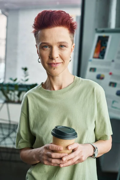 Smiling non-binary person with takeaway drink in paper cup looking at camera in modern office — Stock Photo