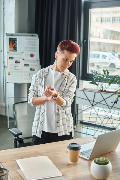 Bigender manager in casual attire standing at workplace and looking at laptop in modern office — Stock Photo