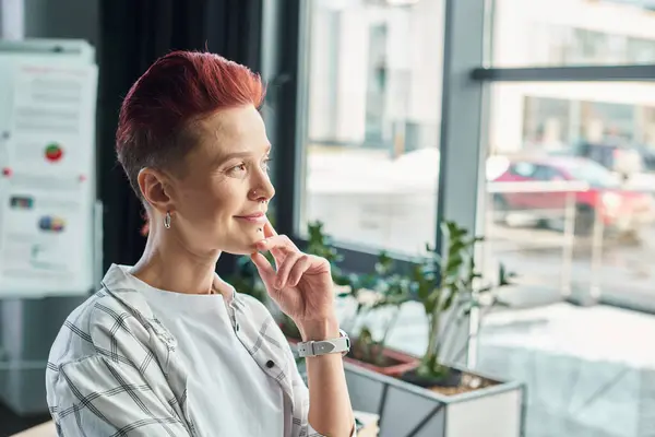 Pensive and smiling non-binary manager in casual attire standing and looking away in modern office — Stock Photo