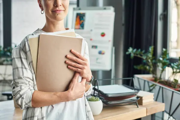 Cropped view of non-binary manager holding folders with documents while standing in modern office — Stock Photo