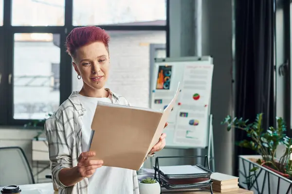 Stylish bigender person in casual attire looking in folder with documents in contemporary office — Stock Photo