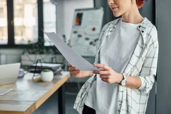 Cropped view of non-binary person in casual attire standing with paper documents in modern office — Stock Photo