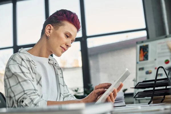 Konzentrierte bigeschlechtliche Person in Freizeitkleidung mit digitalem Tablet bei der Arbeit im modernen Büro — Stockfoto