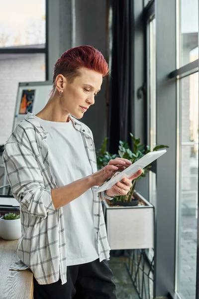 Stylish bigender manager in casual attire standing in modern office and using digital tablet — Stock Photo