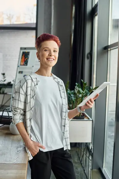 Felice bigender manager in abbigliamento casual in piedi in ufficio con tablet digitale e guardando la fotocamera — Foto stock