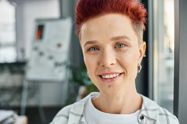 Portrait of cheerful stylish queer person with facial piercing looking at camera in modern office — Stock Photo