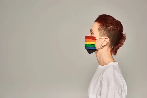 Vista lateral da pessoa queer ruiva em cores do arco-íris máscara médica no fundo cinza, retrato de perfil — Fotografia de Stock