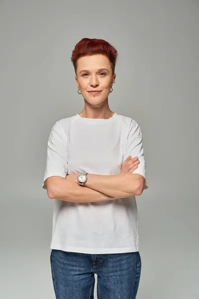 Smiling bigender person in white t-shirt standing with folded arms and looking at camera on grey — Stock Photo