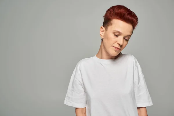 Frustrated and sad redhead bigender person in white t-shirt standing with bowed head on grey — Stock Photo