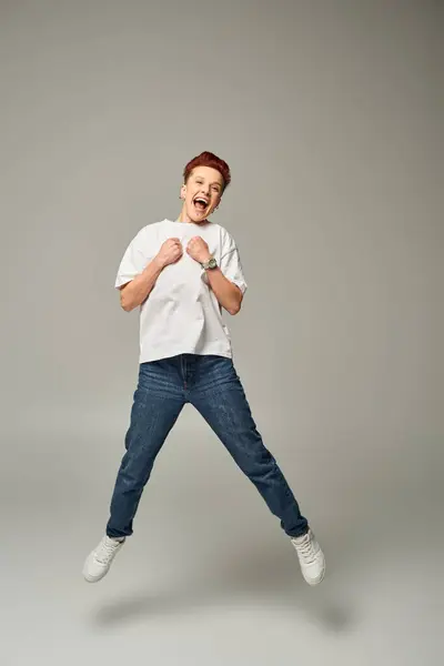 Full length of overjoyed non-binary person in white t-shirt and jeans levitating on grey backdrop — Stock Photo