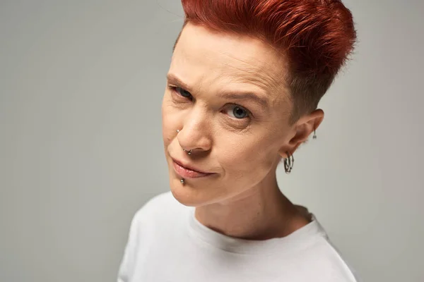 Skeptical and suspicious redhead non-binary person looking at camera on grey studio backdrop — Stock Photo