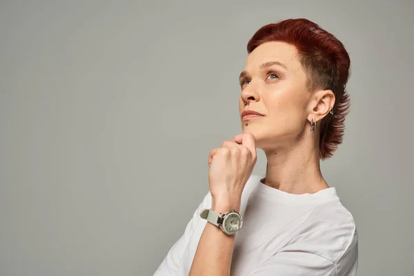Thoughtful redhead non-binary person holding hand near chin and looking away on grey backdrop — Stock Photo