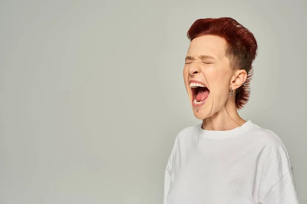 Pessoa queer emocional em branco t-shirt de pé e gritando com os olhos fechados no fundo cinza — Fotografia de Stock