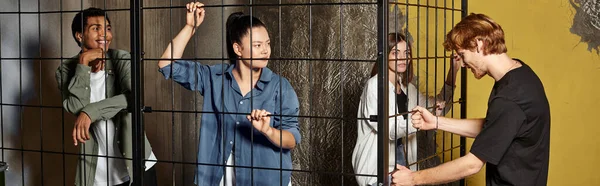 Banner of guy trying to unlock cage in his multicultural friends inside during game in escape room — Stock Photo