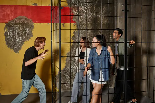 Rothaariger Kerl erschreckt seine multikulturellen Freunde in einem verschlossenen Käfig während eines Spiels im Escape Room — Stockfoto