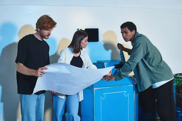 Interracial team holding blueprint and talking during quest in escape room, brainstorming — Stock Photo