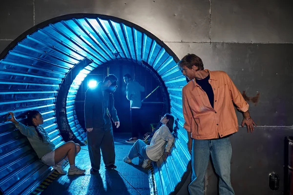 Grupo interracial de amigos participando emocionante aventura en la sala de misiones en el túnel con luz azul - foto de stock