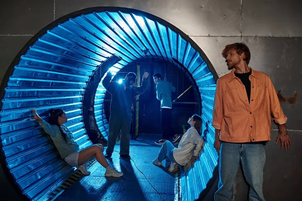Grupo multiétnico de amigos que participan emocionante aventura en la sala de misiones en el túnel con luz azul - foto de stock