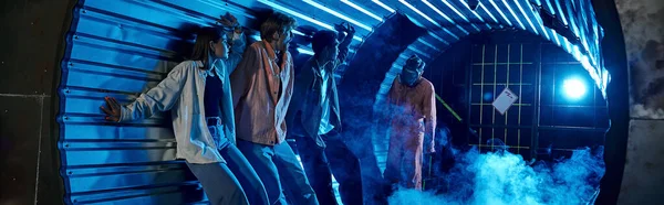 Amis multiethniques debout dans le tunnel près de gens bizarres en masques à gaz, bannière de salle de quête — Photo de stock