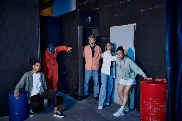 Grupo interracial de amigos escapando de homem com máscara de gás durante a aventura na sala de busca — Fotografia de Stock