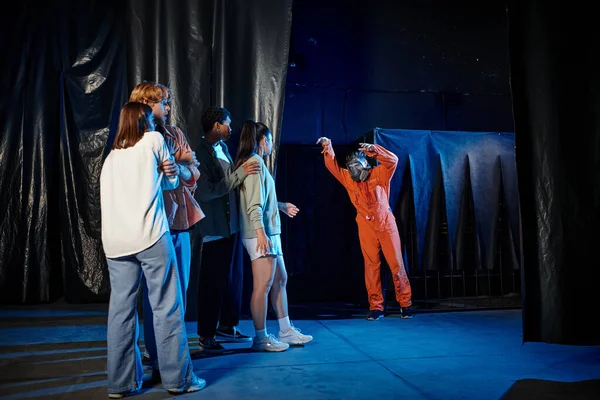 Menschen im Escape Room verstecken sich vor Mann mit Gasmaske und orangefarbenem Anzug — Stockfoto