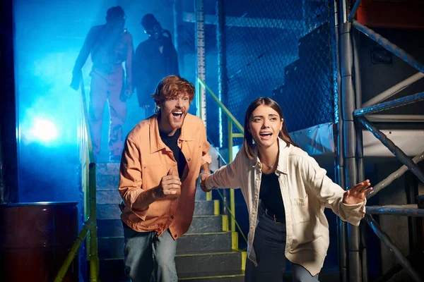 Homem assustado e mulher correndo de pessoas estranhas em máscaras de gás e ternos laranja ppe na sala de fuga — Fotografia de Stock