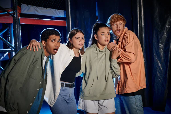 Four diverse and scared young people looking at something while discovering a clue in escape room — Stock Photo